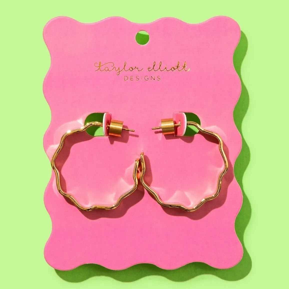 Taylor Elliott Designs gold wavy hoop earrings on pink card